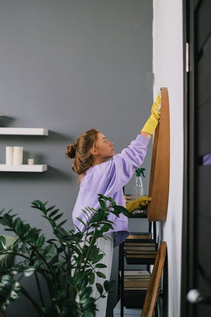 A person wearing brown cleaning gloves is placing a lightbox sign on a white surface that displays the words 'CLEANING HOME' in brown block letters, indicating domestic cleaning services. The backgrou